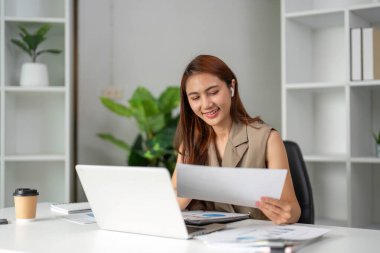Genç bir kadın, modern ofis düzeninde üretkenliğin coşkusunu somutlaştıran tatmin olmuş bir gülümsemeyle belgelerine odaklanıyor..