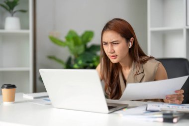 Genç bir kadın yoğun bir şekilde çalışma belgelerini inceliyor, modern ofis ortamında konsantrasyonunu sergiliyor, görevlerini dikkatle yapıyor..