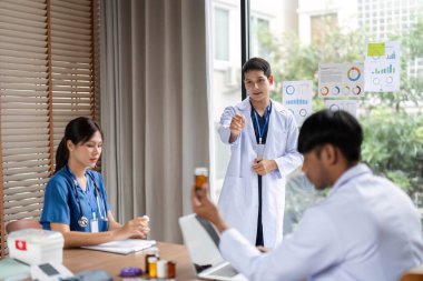 Toplantıda sağlık uzmanlarına eğitim veren bir doktor, masada pratik araçları kullanırken tedavi planlarını vurgular.