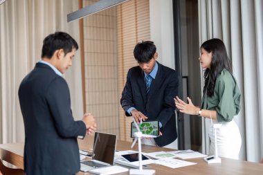 Bir grup profesyonel, bir konferans masasının etrafında dizüstü bilgisayarlar ve yenilenebilir enerji modelleriyle ESG stratejilerini tartışarak sürdürülebilirlik toplantısına katıldı..