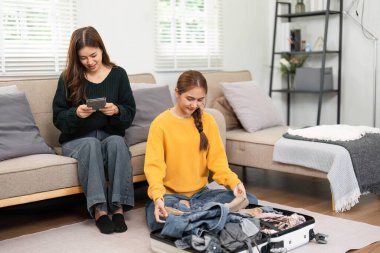 İki arkadaş canlı bir oturma odasında bavullarını topluyor seyahat planlarını tartışıyor ve kahkahalarını paylaşıyorlar..