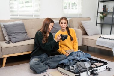 İki kadın fotoğraf incelerken ve seyahat için giysileri toplarken, takım çalışmasını ve arkadaşlığı ön plana çıkarırken aynı anı paylaşıyor..