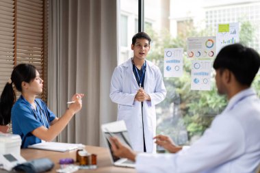 Bir tartışma sırasında bir sağlık ekibine içgörü sunan, işbirliğini teşvik eden ve profesyonel bir çevrede bilgi paylaşan bir doktor.