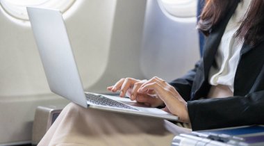 Genç bir iş kadınının elleri uçakta otururken dizüstü bilgisayarda yazarken yakın plan görüntüsü verimliliği vurguluyor..