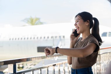 Havaalanında telefonuyla sohbet eden genç bir kadın seyahat heyecanı ve iş hayatının karışımını sergiliyor..
