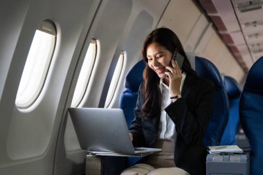 Uçuş sırasında dizüstü bilgisayar kullanan genç bir kadın iş seyahatinde verimliliği vurguluyor..