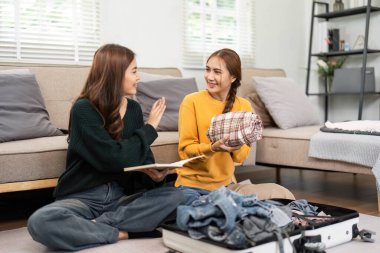 İki arkadaş seyahat çantalarını rahat ve davetkar bir oturma odasına yerleştirirken heyecanlarını ve kahkahalarını paylaşıyorlar..