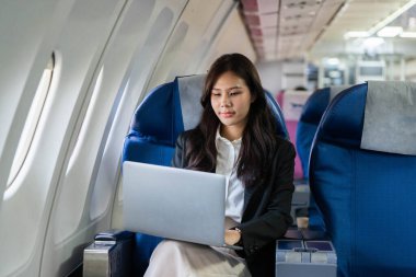 Genç bir iş kadını uçuş sırasında dizüstü bilgisayarı üzerinde çalışırken konsantre olur, üretkenliği ve odaklanmayı somutlaştırır..