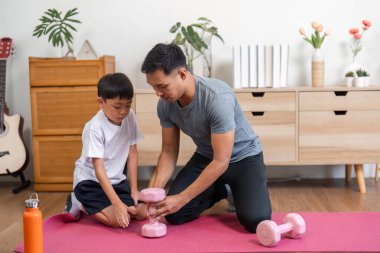 Bir baba ve oğlu birlikte spor yapıyor, egzersiz tekniklerine odaklanıyor ve neşeli ve neşeli bir jimnastik salonunda kaliteli zaman geçiriyor..