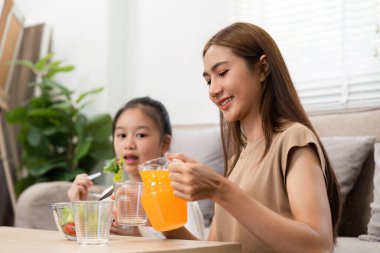 Neşeli bir anne ve kız besleyici meyve sularının ve salatalarının tadını çıkarıyorlar, evde sağlıklı bir yaşam ve refahın altını çizerek aile zamanlarının tadını çıkarıyorlar..