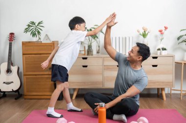 Bir baba ve oğul sıcak ve davetkar bir spor salonunda vücut çalışmalarını kutlayarak beşlik çakar..