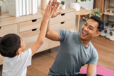 Neşeli bir baba ve oğul evde eğlenceli egzersiz faaliyetlerine girişir, fitness, kahkaha ve güçlü aile bağlarını teşvik eder..
