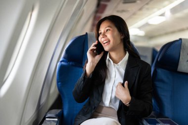 Gülümseyen bir iş kadını uçuş sırasında bir telefon görüşmesi yaparak iş ve seyahat dengesini vurguluyor..
