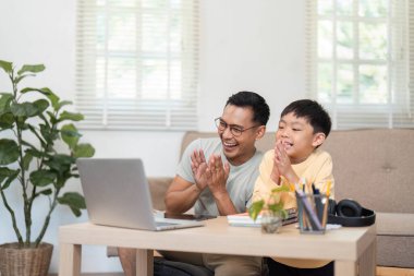 Neşeli bir baba ve oğul evde dizüstü bilgisayarla ders çalışıp eğleniyorlar..