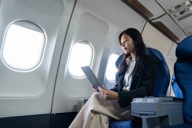Uçuşta tablet kullanan bir iş kadını, rahat bir uçak koltuğunda seyahat ederken verimlilik ve odaklanma örneği gösteriyor..
