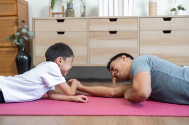 Evde bilek güreşi yapan bir baba ve oğul, kahkahalarını paylaşıyor ve oyun oynayarak aile bağlarını güçlendiriyor..