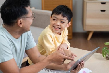 Evde eğitim gören bir baba ve oğul, dijital aktivitelerini tablet üzerinde paylaşıyor, öğrenme ve etkileşimi teşvik ediyor.