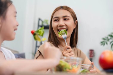Gülümseyen bir anne ve kız besleyici salatalarının tadını çıkarıyor, sağlıklı bir yemek deneyimi sırasında sağlık, neşe ve aile bağlarını destekliyor..