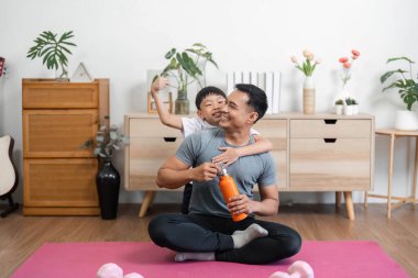 Bir baba ve oğul, spor yaptıktan sonra, birbirlerine eşlik ederken evde sevgi ve beraberlik göstererek sevinçlerini ifade ederler..