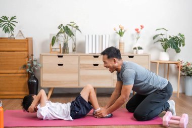 Bir baba evdeki eğlenceli antrenman sırasında oğluna yardım ediyor. Egzersiz yaparken kahkaha ve aile bağı sergiliyor..