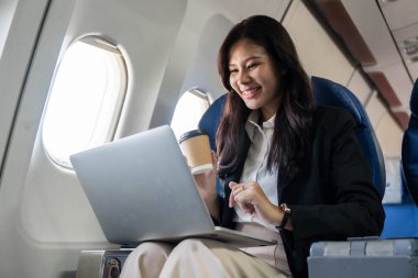 Keyifli bir iş kadını laptopuyla uğraşırken kahvenin tadını çıkartıyor, uçuşun verimliliğini ve memnuniyetini yansıtıyor..