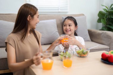 Sağlıklı portakal suyunu paylaşırken gülümseyen bir anne ve kız çocuğu, mutluluğu ve aile anlarını temsil eder..