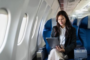 Uçakta tablet kullanan genç bir iş kadını seyahatleri boyunca bağlı ve üretken kalıyor..