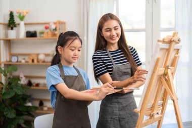 Canlı bir resim oturumunda kızına rehberlik eden destekleyici bir anne, parlak bir stüdyoda yaratıcılığı ve bağlantıyı teşvik ediyor..