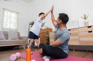 Evde eğlenceli bir spor salonunda bir baba ve oğulun beşlik çakışlarını gösteren neşeli bir an onların bağlarını ve aktivitelerini kutlarken..