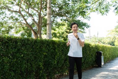 Yaşlı bir adam manzaralı bir park yolunda koşuyor, zindelik ve sağlığa olan bağlılığını somutlaştırıyor..