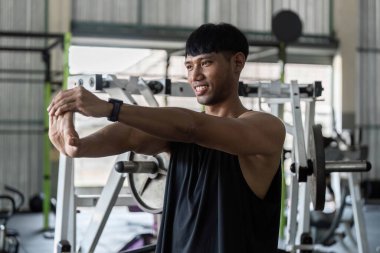 Odaklanmış genç bir adam spor salonunda esneme egzersizi yapıyor. Formda ve sağlıklı olduğunu vurguluyor. Sağlık ve egzersiz temaları için ideal.