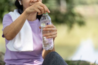 Bir kadın, dışarıda egzersiz yaptıktan sonra su ve sağlık durumunu vurgulayarak şişeden su içmeye hazırlanıyor..