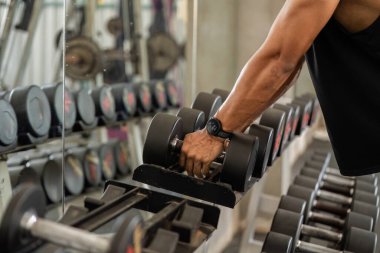 Odaklanmış bir adam, spor salonunda bir dambılı kavrayıp, fitness eğitimine bağlılığını ve gücünü gösterir..