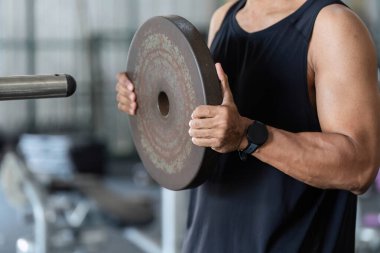 Genç bir adam ağırlık levhasını kaldırıp spor ve fiziksel sağlığa olan bağlılığını göstererek güç antrenmanına başlıyor..