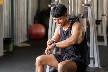 Spor salonundaki neşeli bir adam spor saatini kontrol ediyor, gelişimi kutluyor ve spor yolculuğunun tadını çıkarıyor..