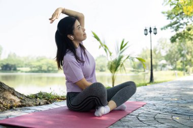 Bir kadın yoga minderinde yan esneme hareketi yapıyor, dışarıda huzurlu bir ortamda sağlığını ve esnekliğini arttırıyor.