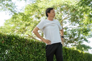 Yaşlı bir adam parkta kollarını uzatarak sağlığını ve fiziksel kondisyonunu arttırıyor. Etkin yaşam tarzı ve sağlığın vurgulanması.