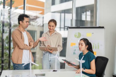 ESG stratejilerini, grafik ve sürdürülebilir iş uygulamaları hakkındaki verileri parlak bir ofiste tartışan çeşitli bir ekip.