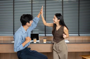 Parlak bir ofis alanında başarılı bir işbirliğini kutlayan iki genç profesyonel beşlik çakıyor..