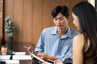 İki meslektaş arasında yapılan bir iş toplantısında, modern bir ofis ortamında mali tablolar ve stratejiler gözden geçirildi..