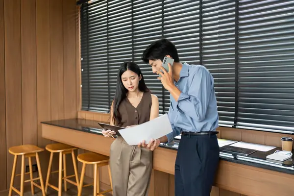 Bir iş kadını ve işadamı proje belgelerini birlikte analiz ediyor, modern bir çalışma alanında takım çalışması ve işbirliği sergiliyor.