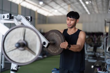 Kendini adamış bir erkek sporcu, modern bir spor salonunda ağırlık kaldırmaya odaklanır..