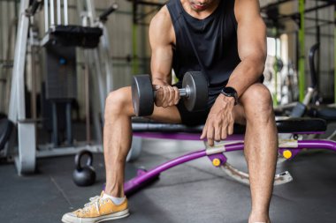 Genç bir adam dambıl kıvırma hareketi yaparken şekline odaklanır. Güç eğitimine ve formda kalmaya özen gösterir..