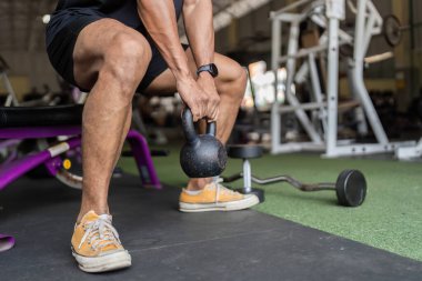 Genç bir adam spor salonunda bir çaydanlık çanı kaldırırken güç ve odaklanma gösteriyor..