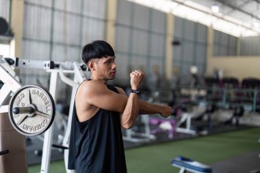 Genç bir adam spor salonunda kol esnetme hareketleri yapıyor, vücut geliştirme ve esnekliğine odaklanıyor, yoğun bir antrenmana hazırlanıyor..
