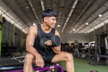 Dambılı kaldırırken gülümseyen genç bir adam spor ve güç eğitimine karşı olumlu bir tavır sergiliyor..