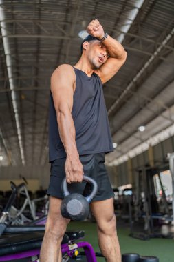 Genç bir adam spor salonunda kettlebell egzersizi yaparak gücünü ve uygunluğunu sergiliyor..