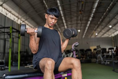 Odaklanmış genç bir adam spor salonundaki biseps için halterleri kaldırıyor, fitness ve güç eğitimine olan bağlılığını gösteriyor..