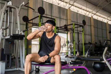 Spor salonundaki yoğun bir çalışmadan sonra bir adam serinletici bir su içer. Sıvı alma ve sağlığa dikkat çeker..