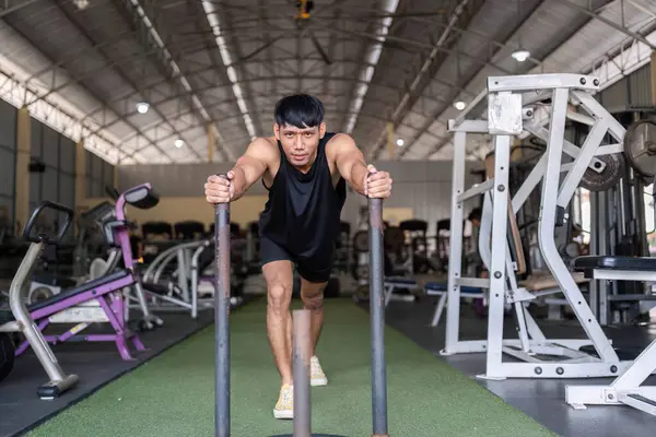 Genç bir adam spor salonunda ağırlıklı bir kızağı itiyor. Gücünü, dayanıklılığını ve kondisyonunu gösteriyor..